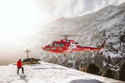 白天，红色直升机在雪山上空飞行